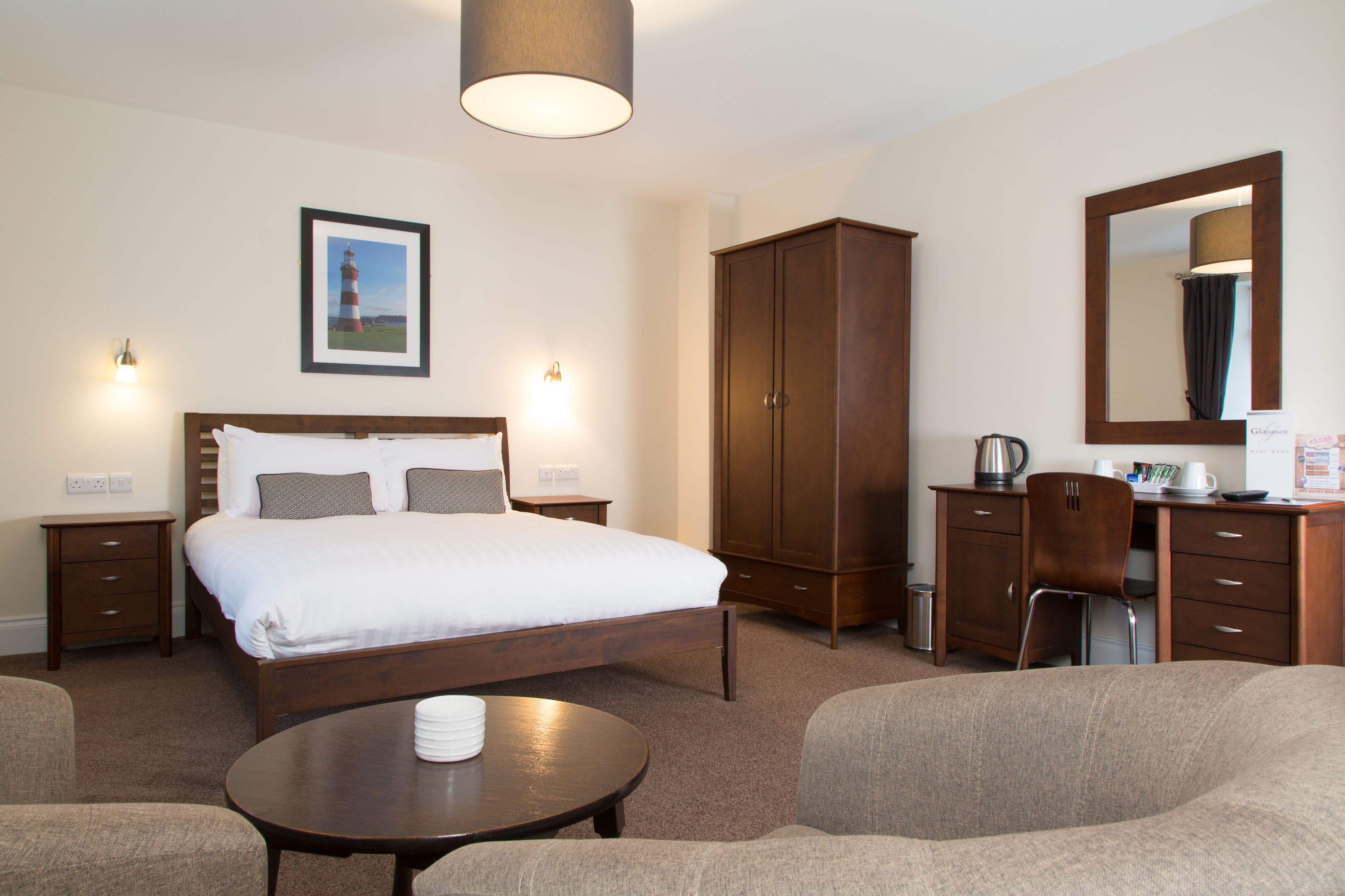 Quarto de hotel com uma cama grande, um guarda-roupa de madeira, uma escrivaninha com cadeira e uma mesa redonda.