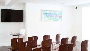 Un salón de conferencias con diseño moderno, que cuenta con un techo blanco, un televisor de pantalla plana montado en la pared y un cuadro abstracto de gran tamaño.