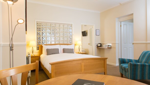 Een hotelkamer met een bed, nachtlampjes, een houten tafel, een stoel en een televisie aan de muur.