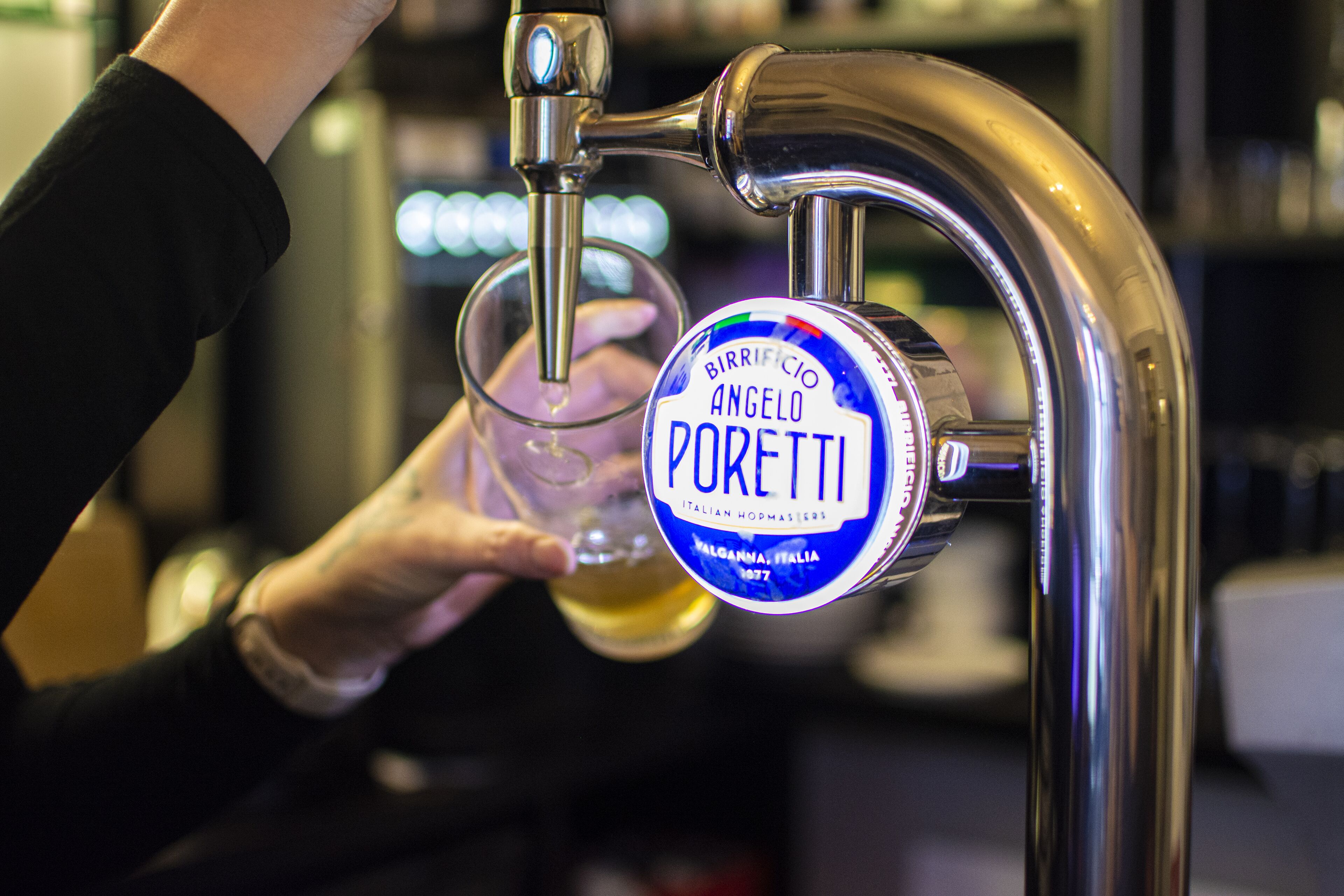 A hand holding a beer glass under a tap labeled "BIRRIFICIO ANGELO PORETTI".