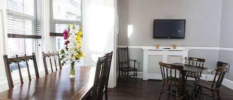 A dining area with a wooden table and chairs, a vase of flowers, and a television mounted on the wall.