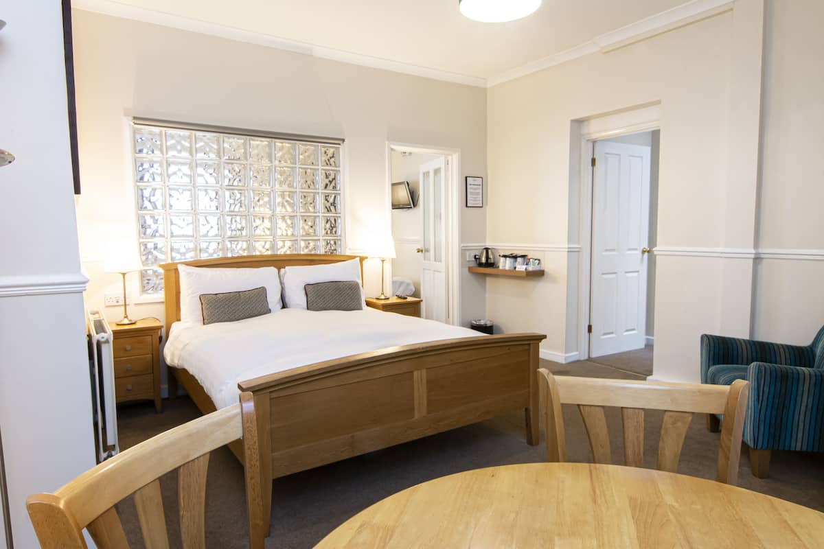 A bedroom with a wooden bed, a bedside table, a lamp, a chair, and a small table.