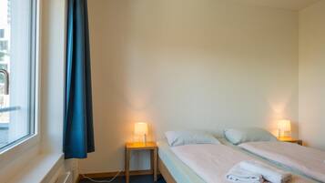 Habitación de hotel con una cama, dos mesitas de noche con lámparas, una ventana con cortina y vistas al exterior.