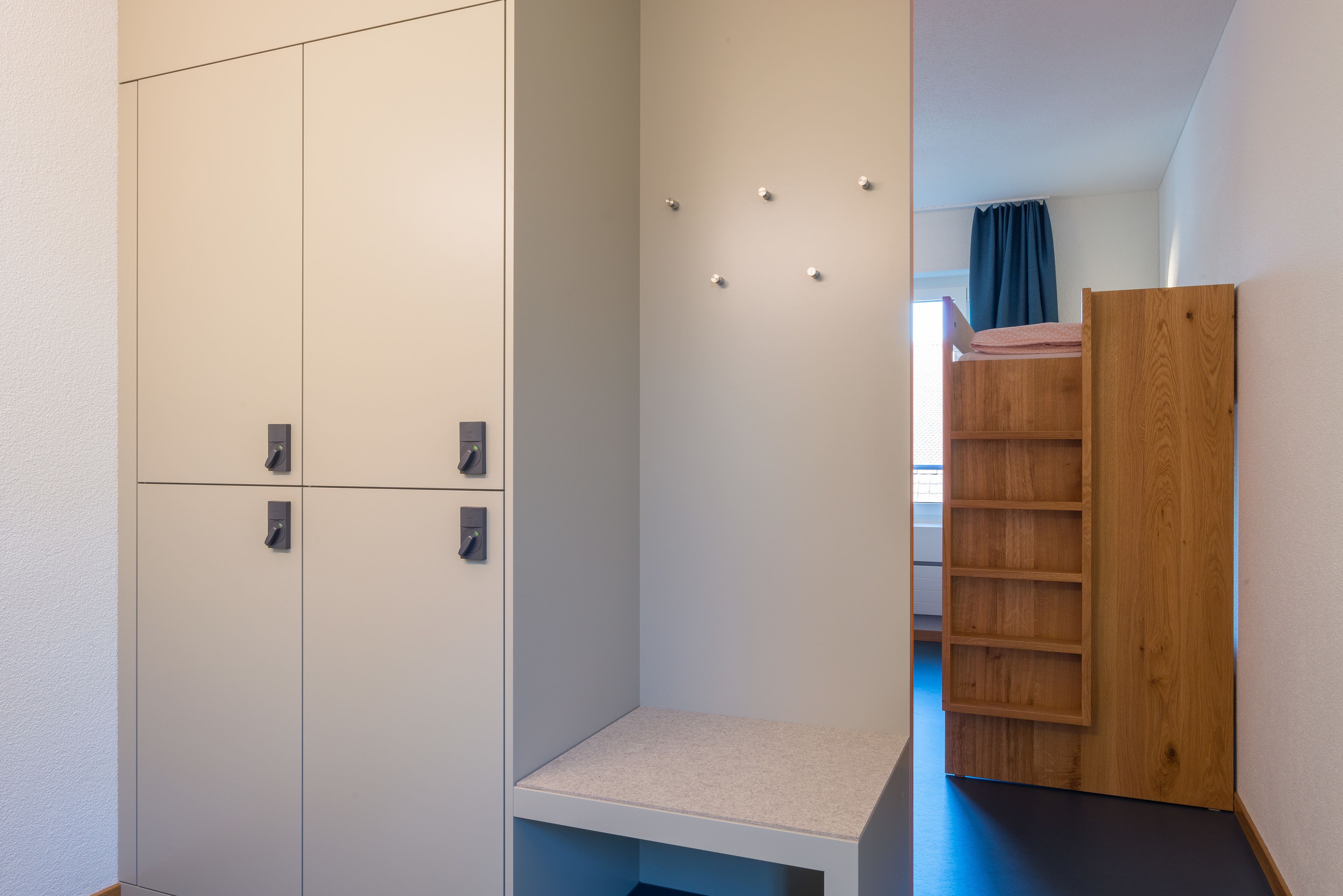 A bedroom with a wardrobe, a small seating area, and a bunk bed.