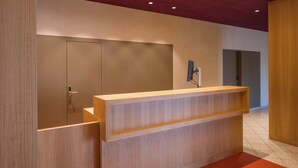 A reception desk with a wooden finish, a wall-mounted TV, and a door with a handle.