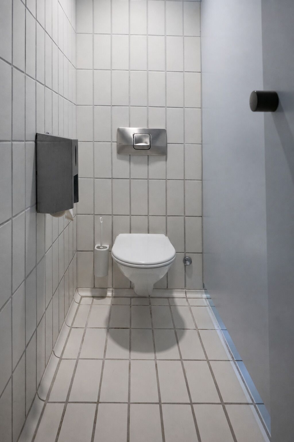 Une petite salle de bain moderne, avec des carreaux blancs, des toilettes, un sèche-mains et une poubelle.