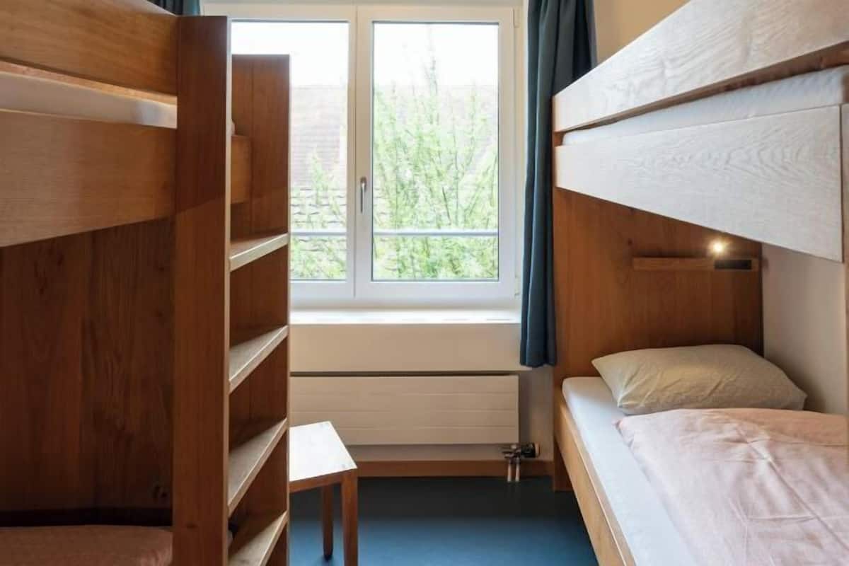 Habitación con literas, una ventana, una mesita pequeña y un radiador.