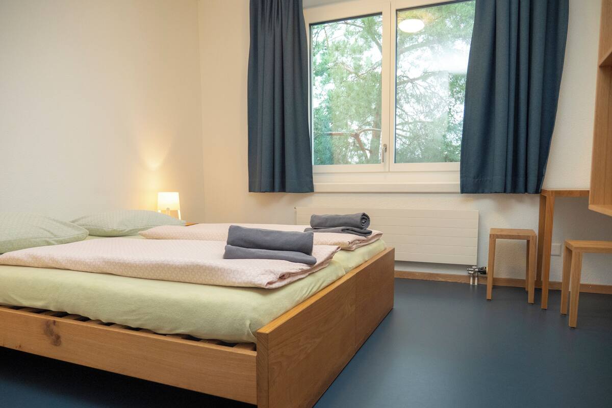 Un dormitorio con una cama de madera, un escritorio pequeño y una ventana con cortinas.