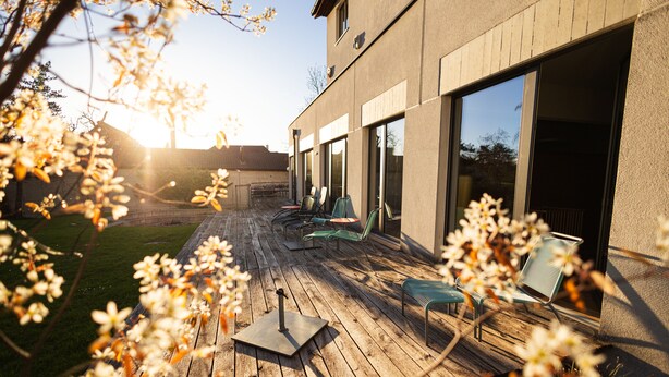 A wooden deck with outdoor furniture, a patio umbrella, and a view of a modern building with large windows.