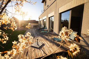 A wooden deck with outdoor furniture, a patio umbrella, and a view of a modern building with large windows. - Youth Hostel Zug (Zug)