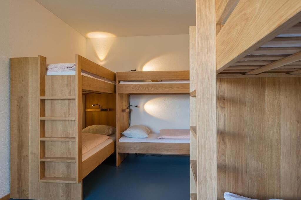 Habitación con literas, una escalera de madera y una estantería.