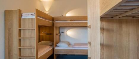 Habitación con literas, una escalera de madera y una estantería.