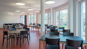 A spacious dining area with multiple tables and chairs, large windows, and ceiling lights.