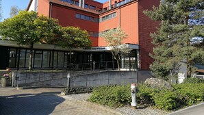 A red-brick building with a modern design, featuring large windows and a covered entrance area.