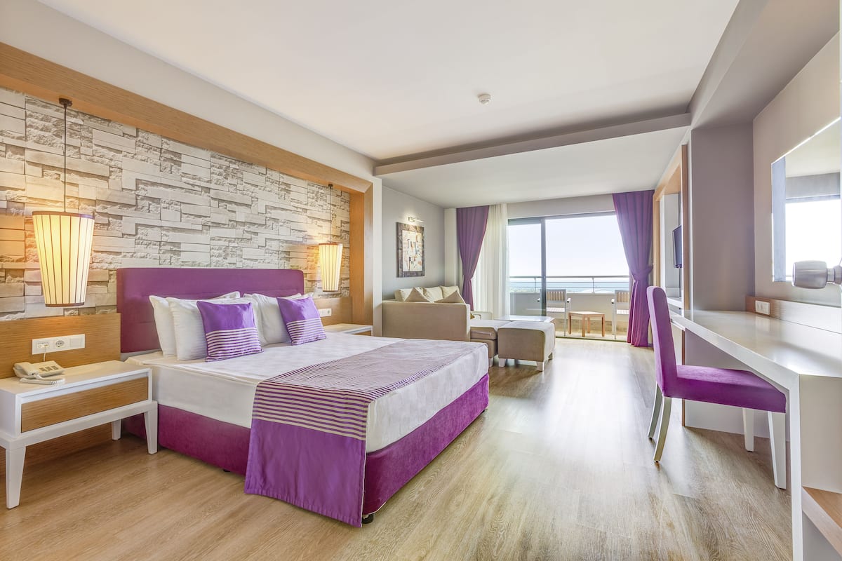A modern hotel room with a large bed, a desk, and a balcony.