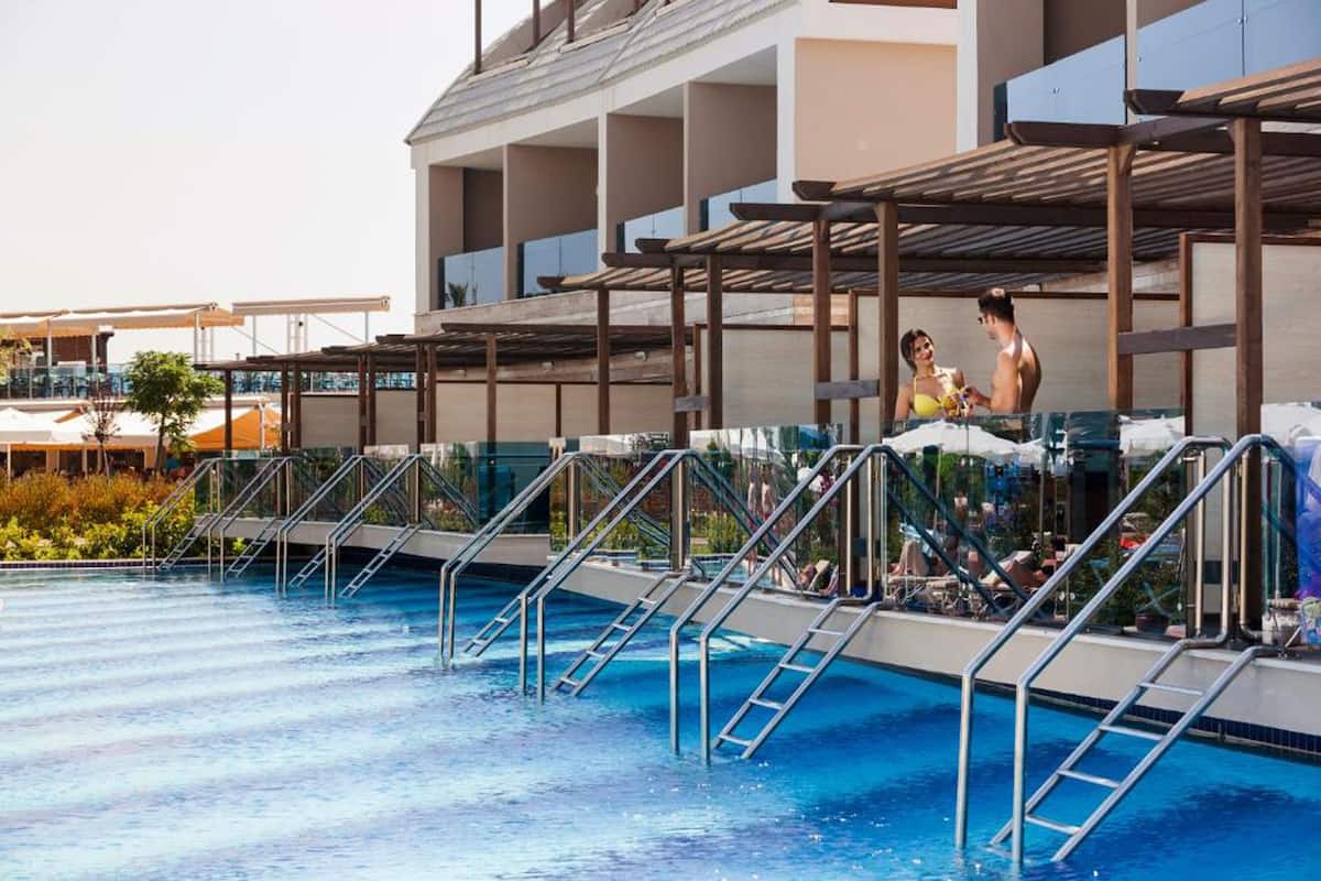 A swimming pool with multiple diving platforms and ladders, surrounded by a covered area with seating and umbrellas.