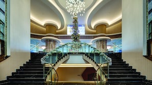 Un lobby espacioso con una escalera central, un gran candelabro y un árbol de Navidad.