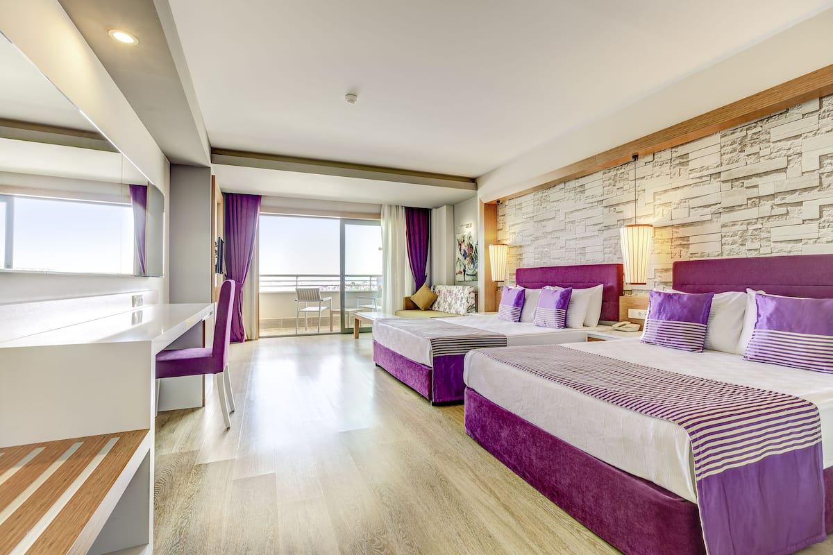 A modern hotel room with two beds, a desk, and a balcony with a view.