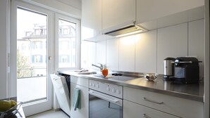 Eine moderne Küche mit integriertem Backofen, einer Mikrowelle und einer Kaffeemaschine. Ein Fenster sorgt für natürliches Licht und bietet einen Blick auf die umliegenden Gebäude.