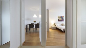 Ein modernes Hotelzimmer mit Holzboden, einer Essecke mit Tisch und Stühlen, einem Bett mit weißem Kopfteil und einem Bild an der Wand.