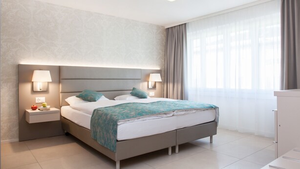 Una camera d'hotel moderna con un letto, comodini e un'ampia finestra con tende.