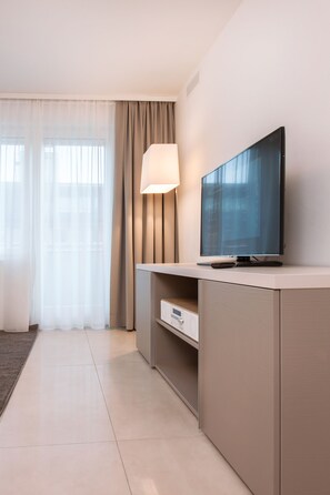 Quarto de hotel moderno com televisão de tela plana em um móvel, uma luminária e vista da cidade através de grandes janelas.