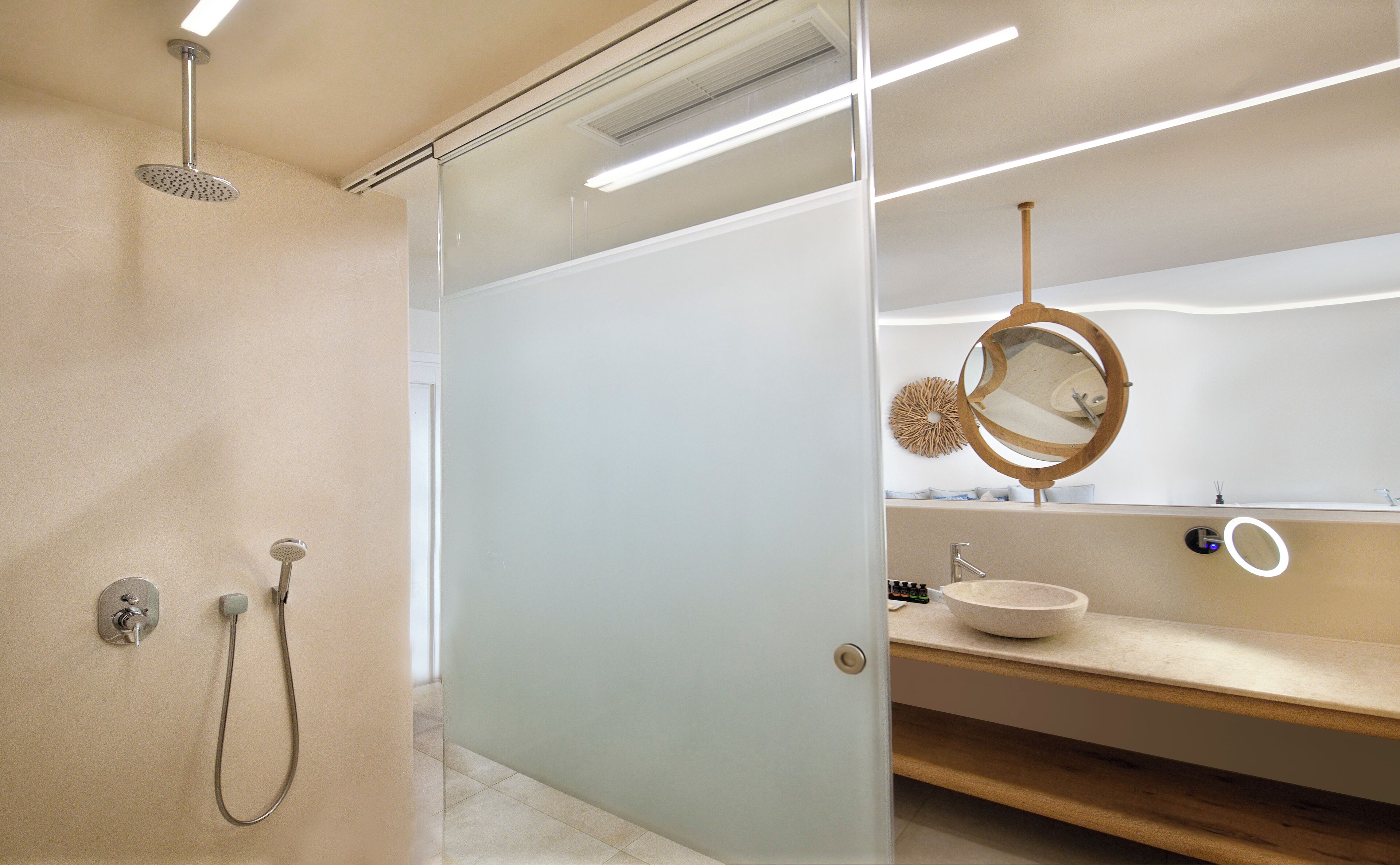 Un baño moderno con cabina de ducha de vidrio, tocador de madera con lavabo y espejo redondo.