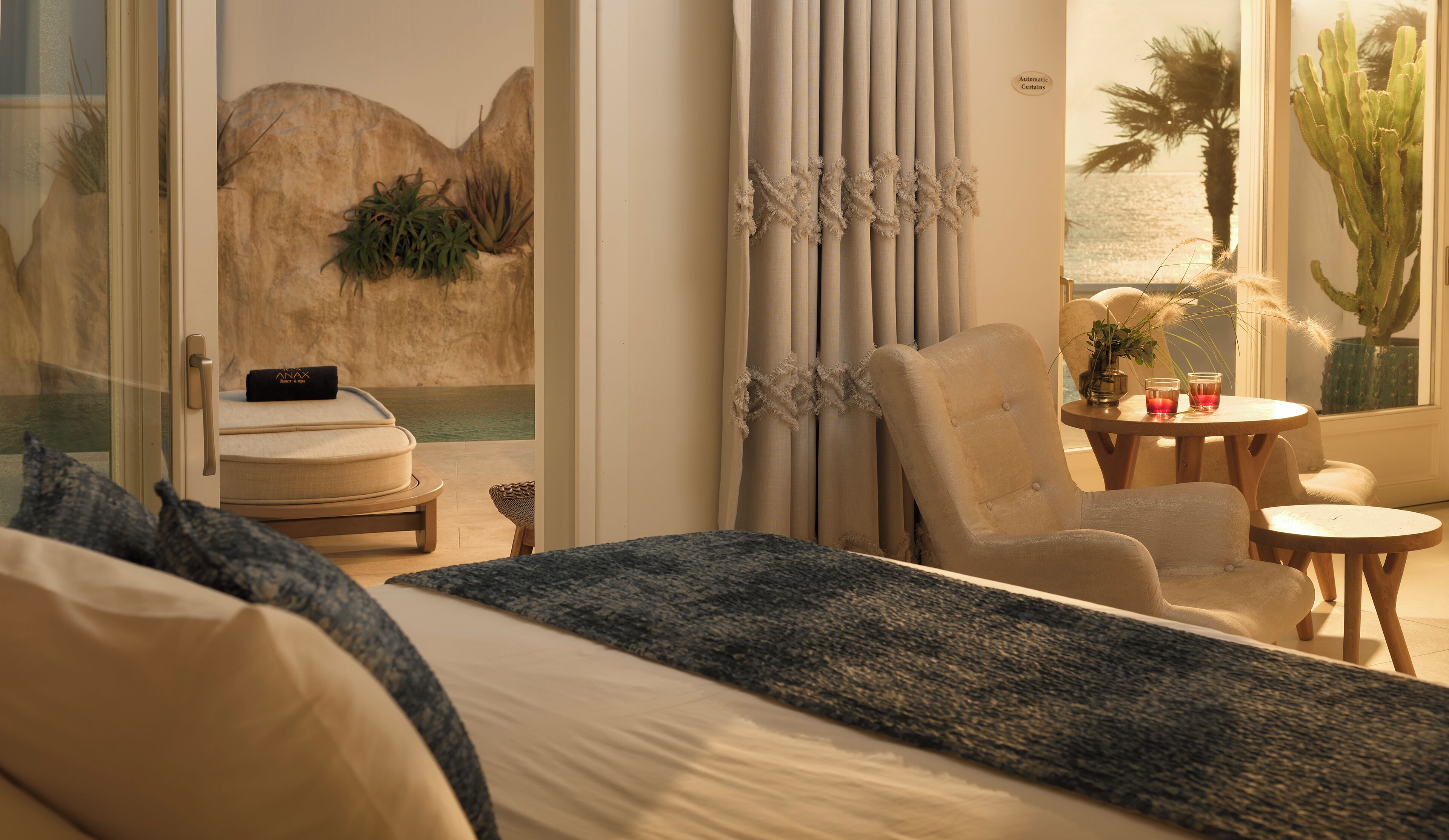 A bedroom with a bed, a chair, a small table, and a view of the ocean through the window.