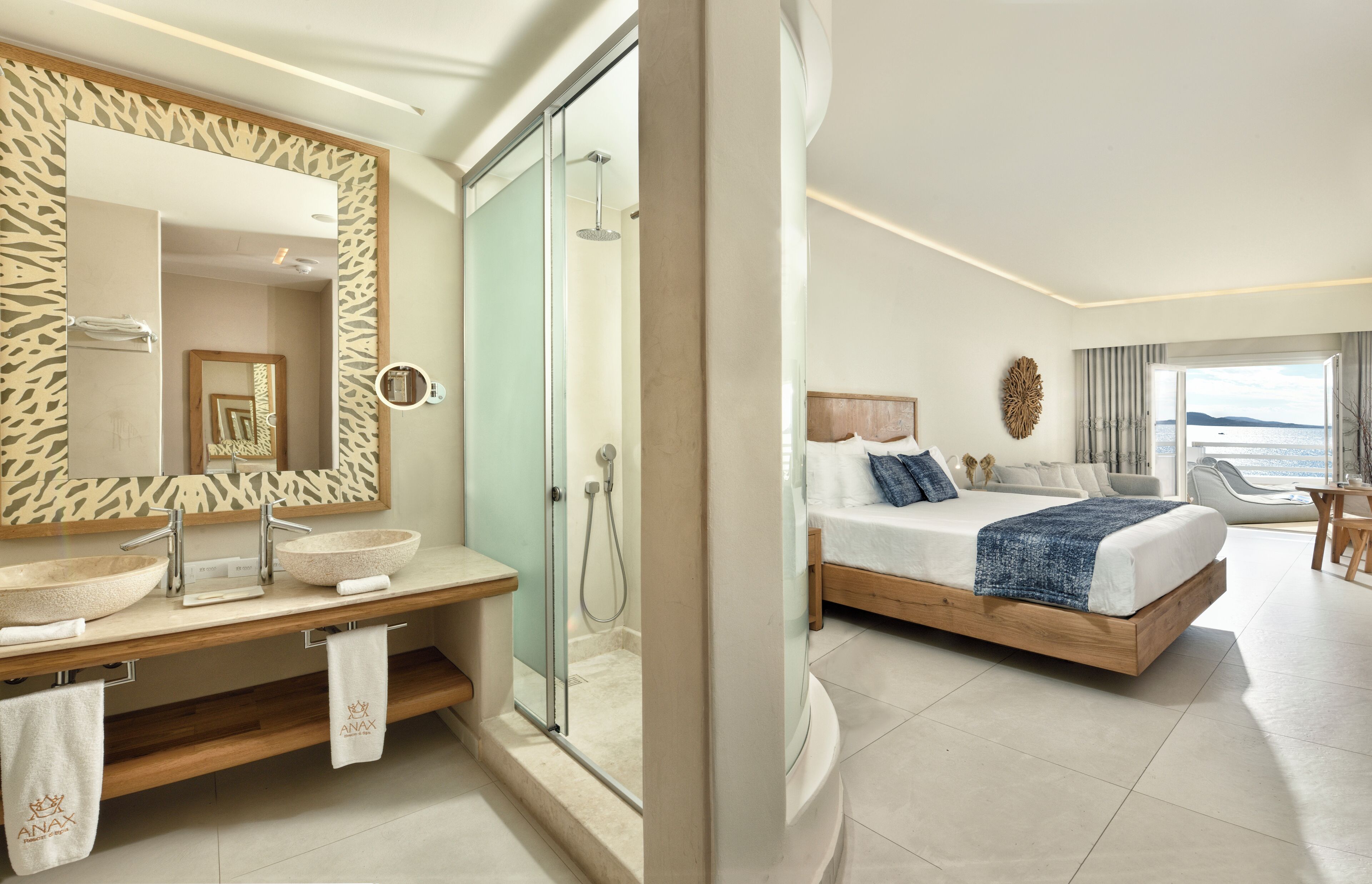 A modern hotel room with a large bed, a bathroom with a vanity and a glass shower enclosure.