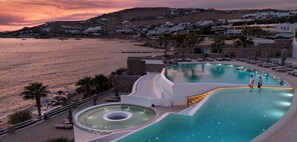 A resort pool with a view of the sea and a hillside of white buildings.