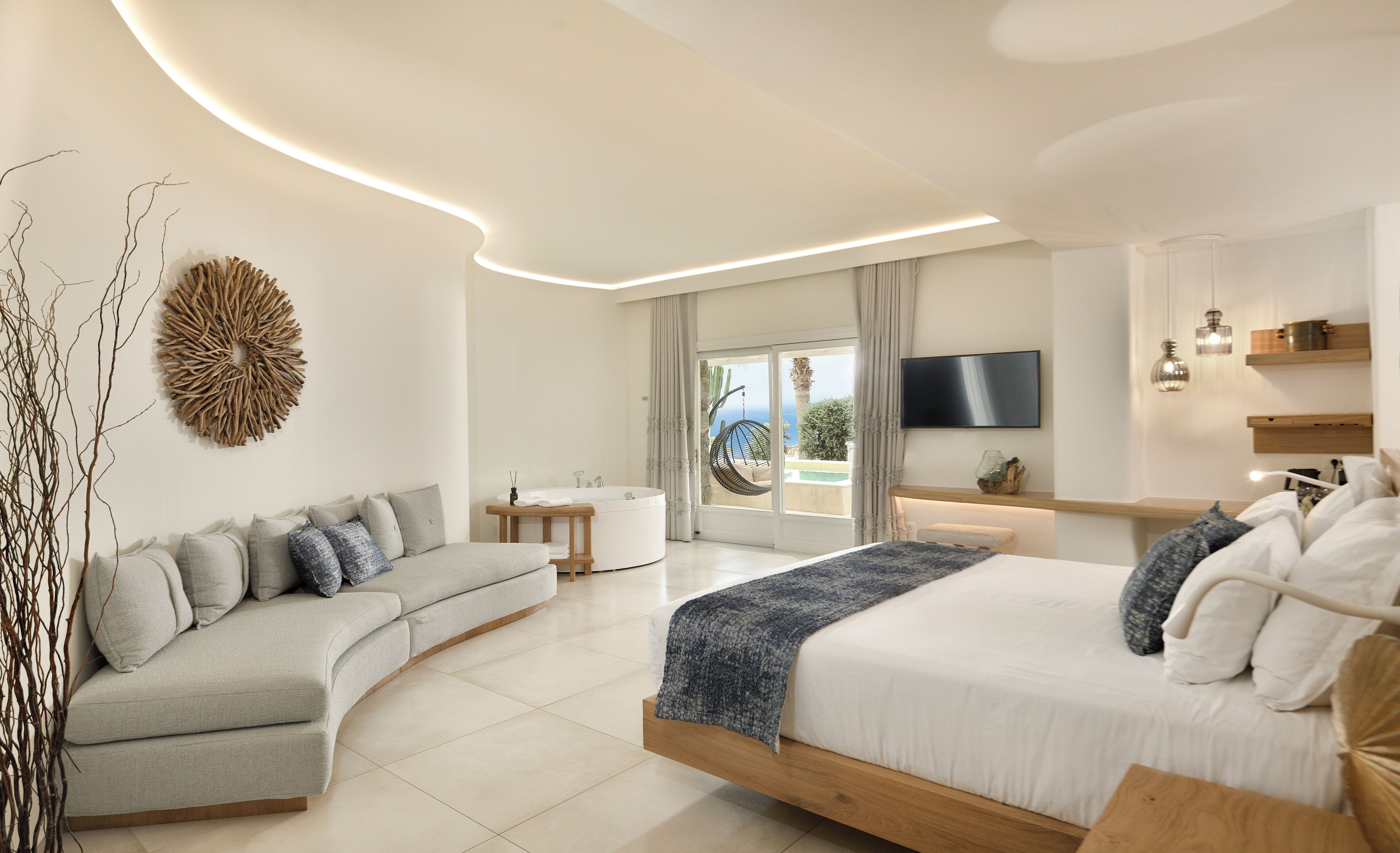 Un dormitorio moderno con un sofá curvo, una cama con estructura de madera, un televisor montado en la pared y vistas al exterior.