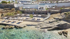 An aerial view of a coastal resort with a clear pool, sun loungers, and umbrellas. - Anax Resort & Spa (Mykonos)