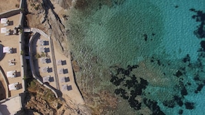 An aerial view of a beachside resort with sun loungers and umbrellas arranged along the shoreline. - Anax Resort & Spa (Mykonos)