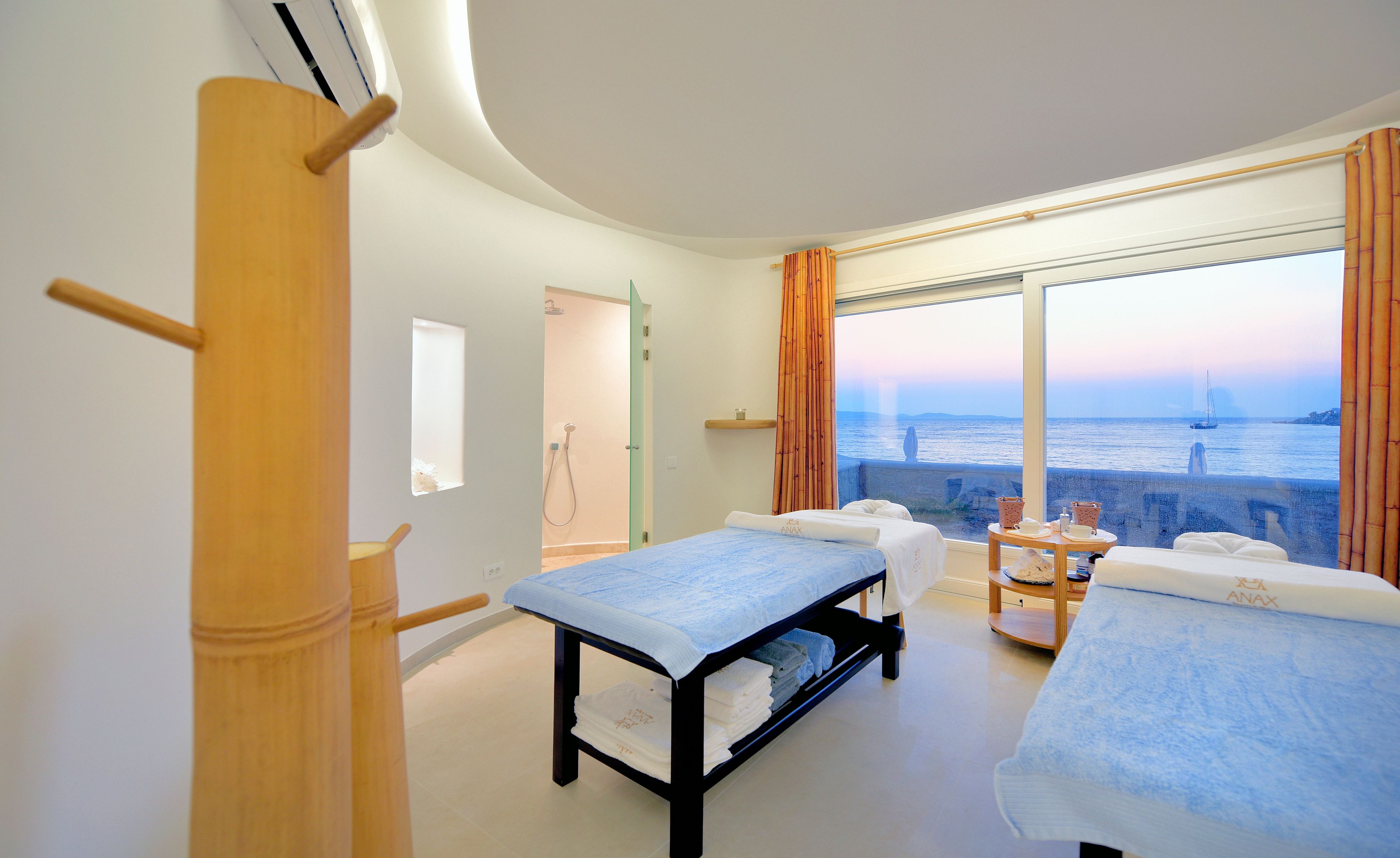 A room with two beds, a window with a view of the sea, and a wooden pillar.