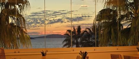 A dining area with a view of the ocean and palm trees at sunset.