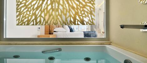 Un baño moderno con un jacuzzi de vidrio, un banco de madera y un panel decorativo en la pared.