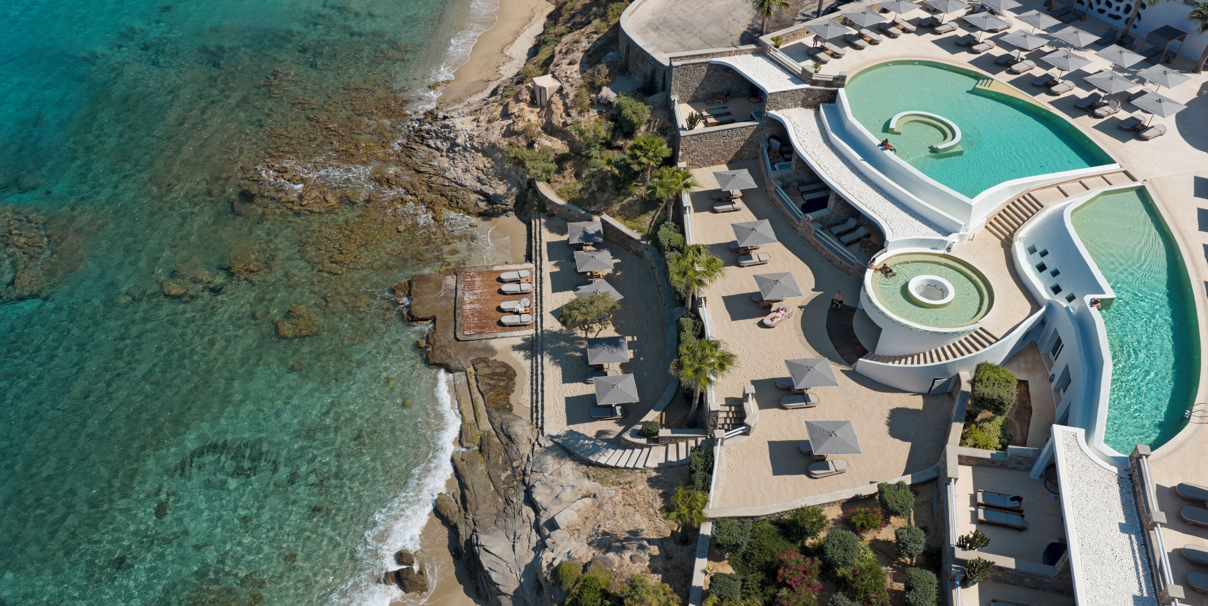 Vista aérea de un resort con piscina, zonas de descanso y una playa.