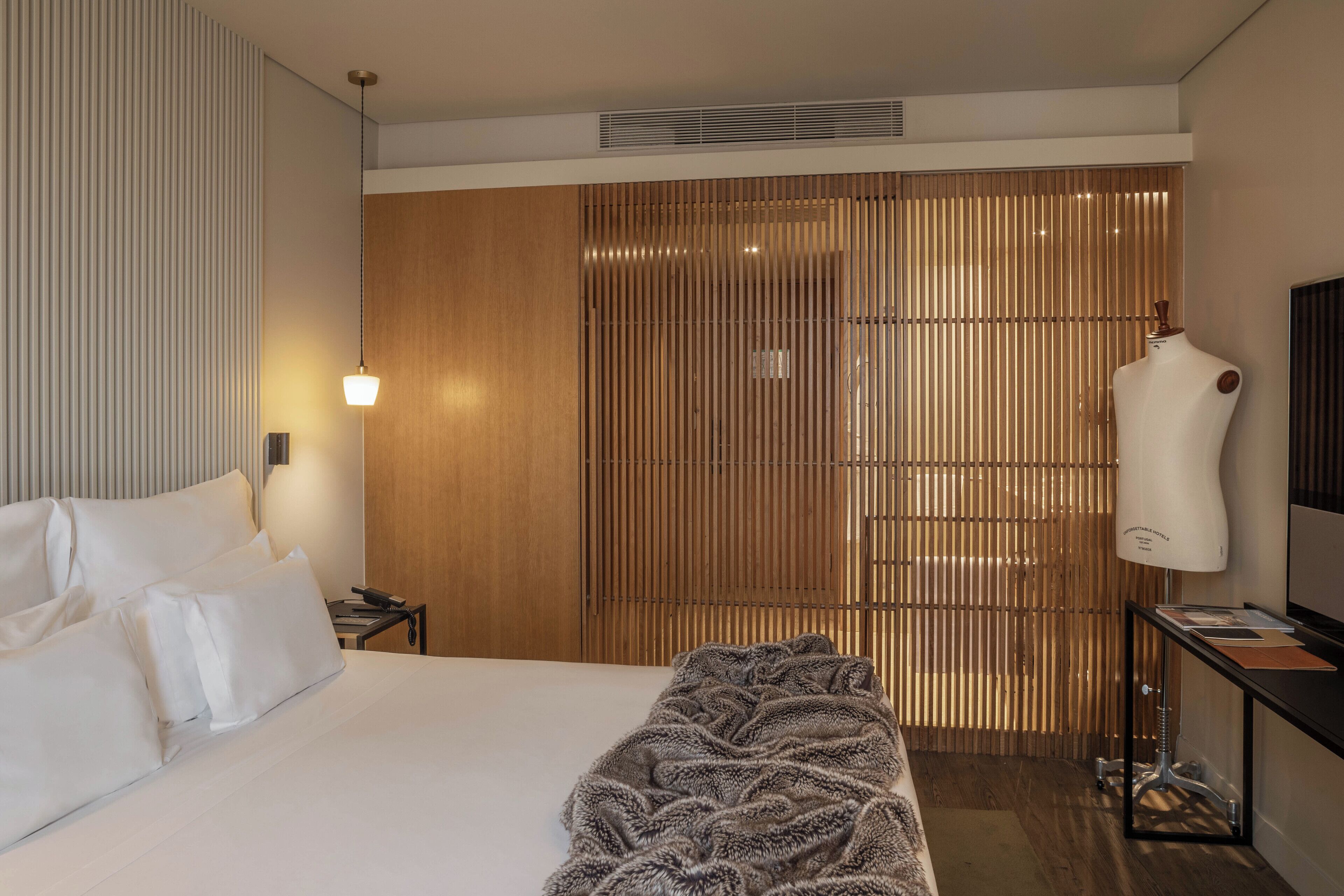 A hotel room with a large bed, a bedside table with a lamp, a wardrobe, and a mannequin.