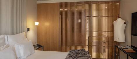 A hotel room with a large bed, a bedside table with a lamp, a wardrobe, and a mannequin.