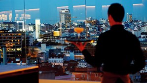 A man holding a tray with a drink, overlooking a cityscape with buildings and a construction crane. - Memmo Príncipe Real - Design Hotels (Lisbon)