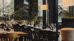A restaurant interior with tables set for dining, chairs, and a large window with plants outside. - Memmo Príncipe Real - Design Hotels (Lisbon)