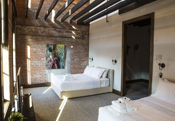Ein Hotelzimmer mit Backsteinwand, einem großen Bett, einem kleineren Bett und einem Gemälde an der Wand.
