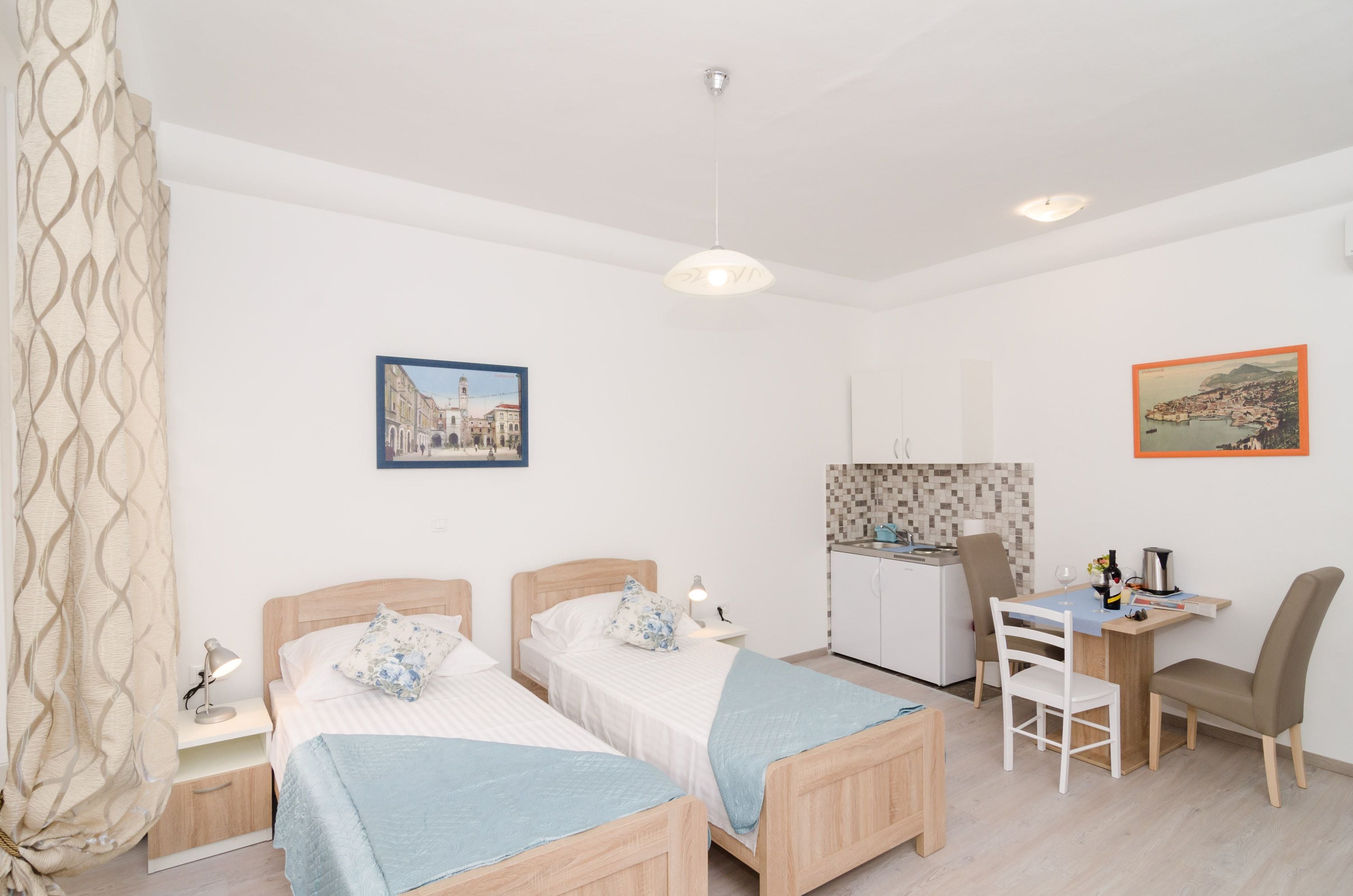 A bedroom with two beds, a desk, and a kitchenette.