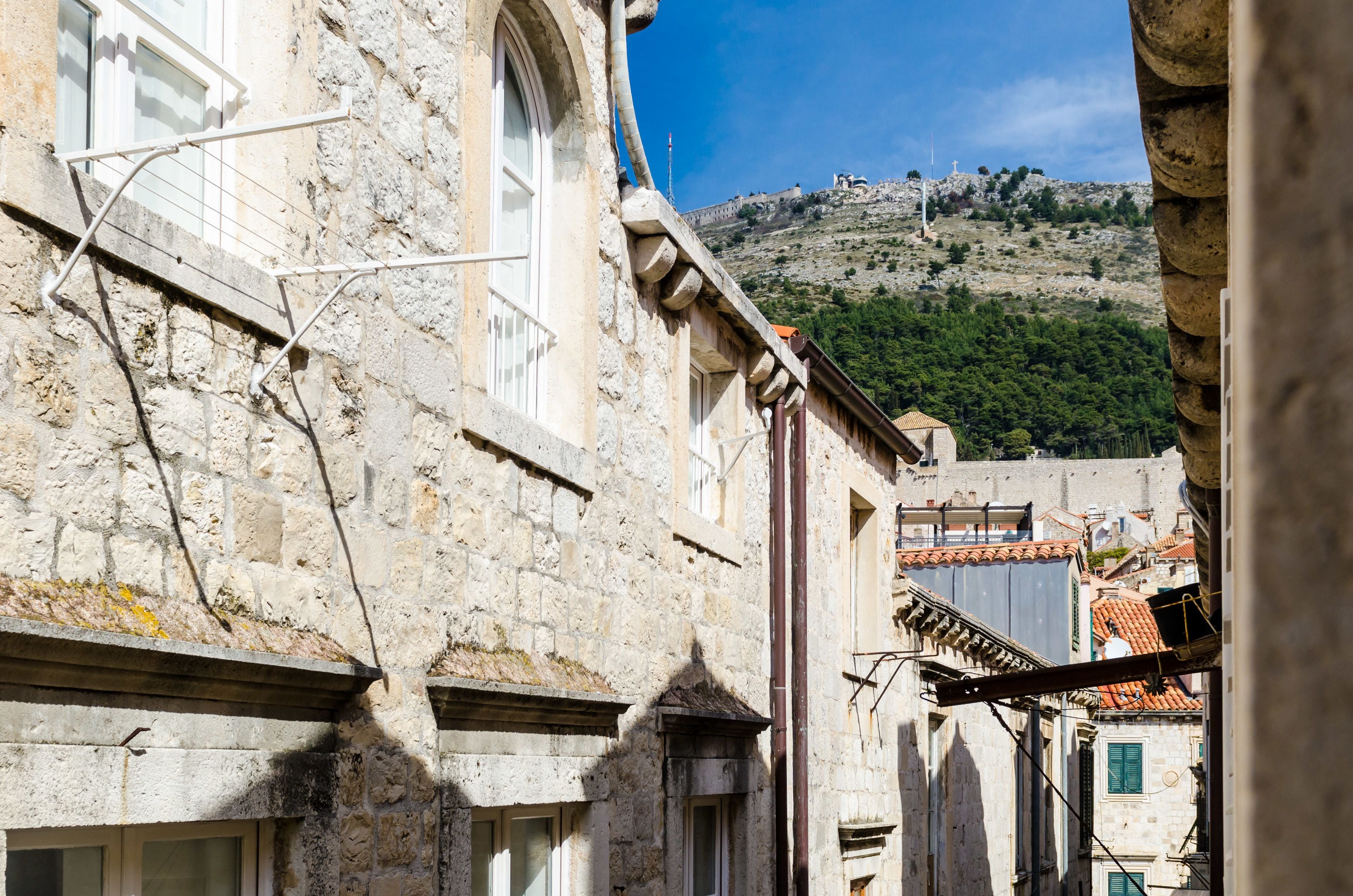 A narrow street with stone buildings, a view of a hill with a fort, and a clear blue sky.