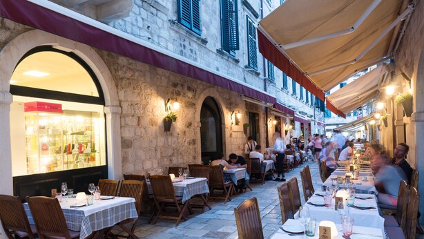 An outdoor dining area with tables set for two, stone walls, and hanging plants. - Rooms Tezoro (Dubrovnik)