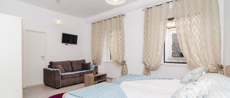 Un dormitorio moderno con dos camas, un sofá, un televisor y una ventana con cortinas.