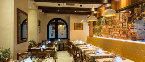 A restaurant with multiple tables set for dining, wooden beams on the ceiling, and a mural on the wall.