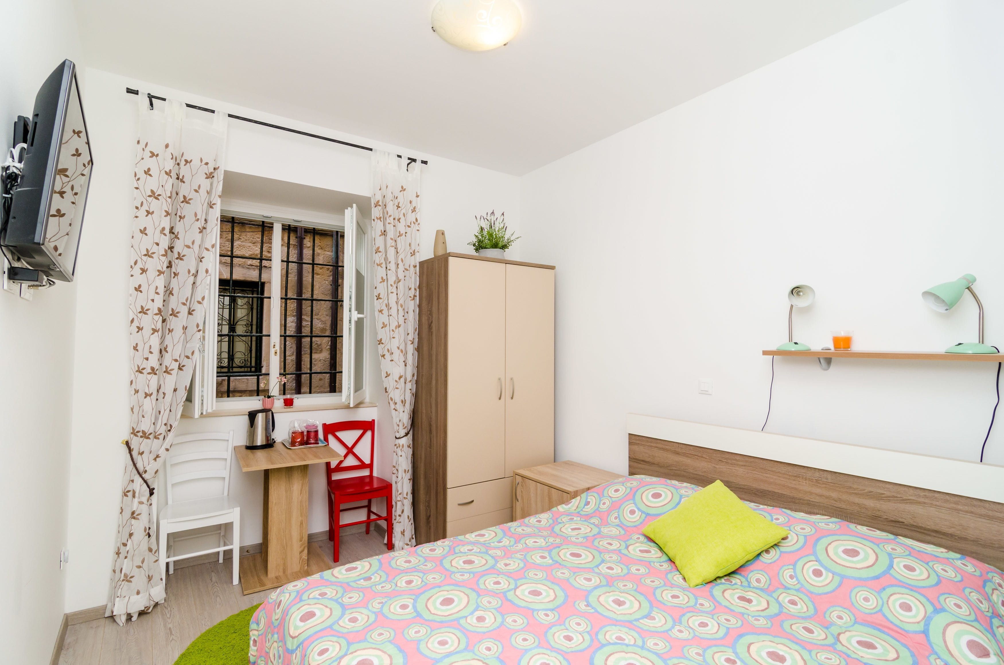 Une chambre à coucher comprenant un lit, un bureau, une chaise, une armoire et un téléviseur fixé au mur.