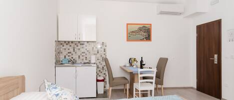 A compact room with a bed, a small kitchenette, a dining area, and a wooden door.