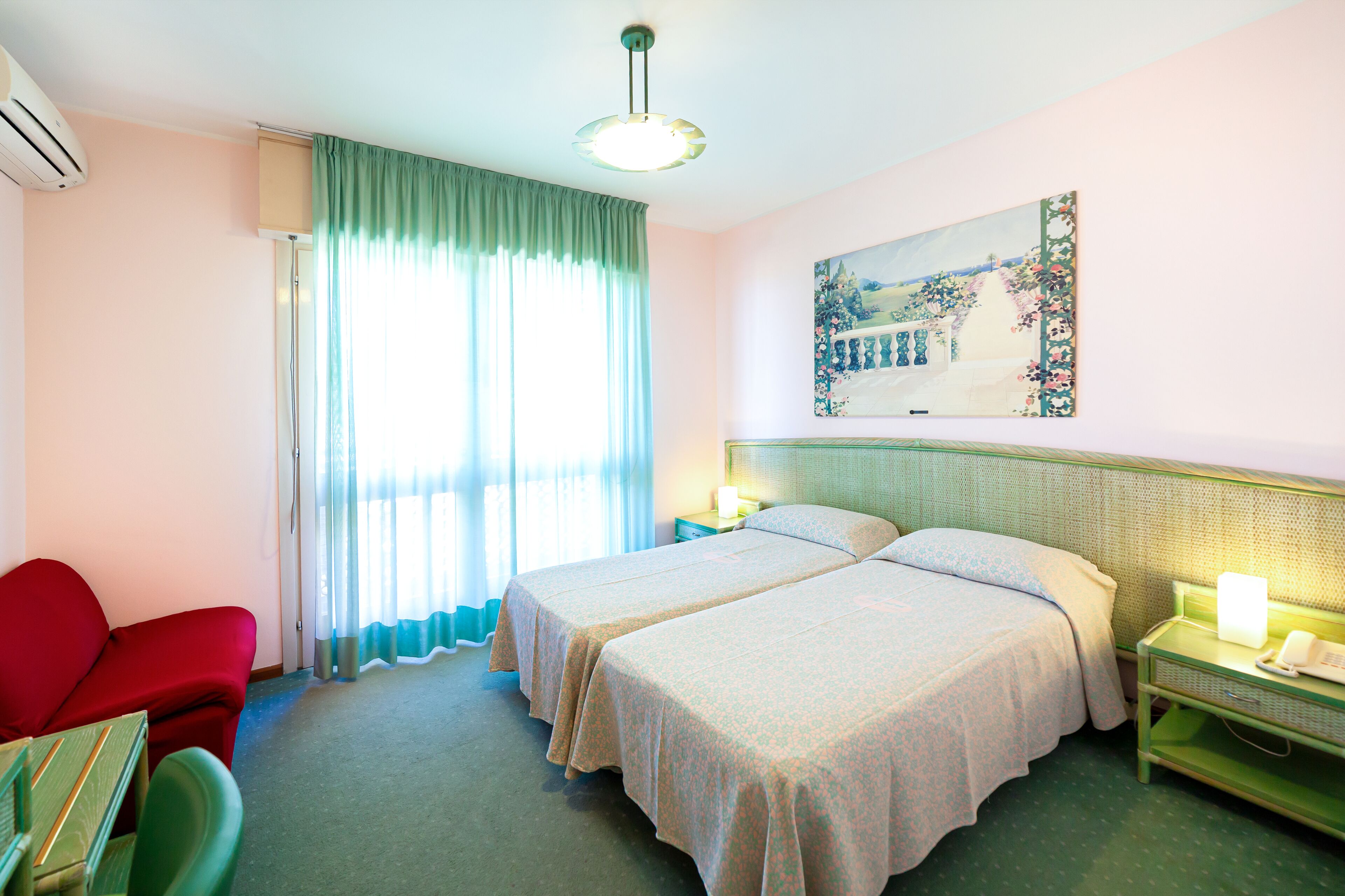 A hotel room with two beds, a red sofa, a small table, and a painting on the wall.